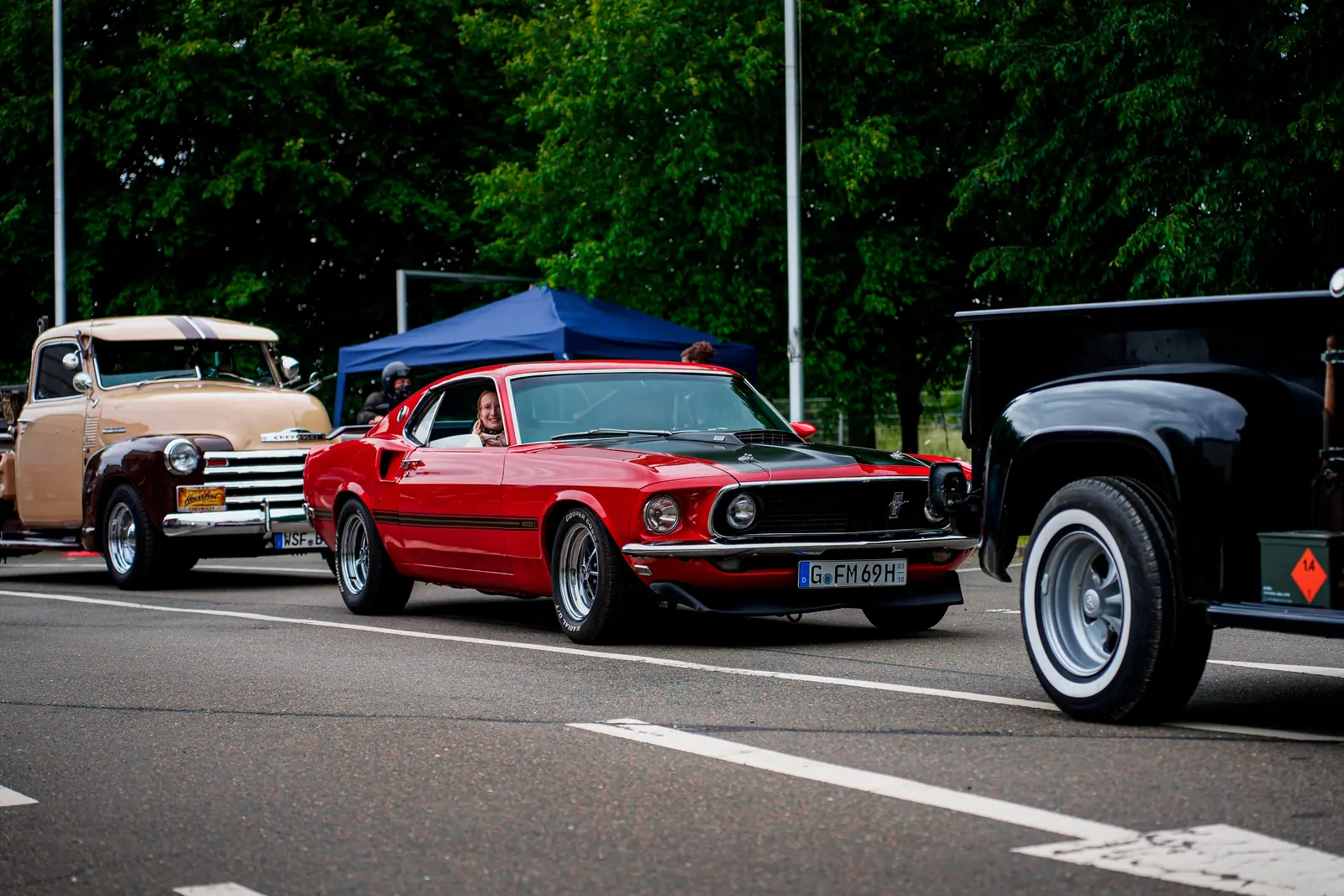 Roter Ford Mustang aus den Sechzigern fährt ein, daneben ein alter Chevrolet-Pick-up
