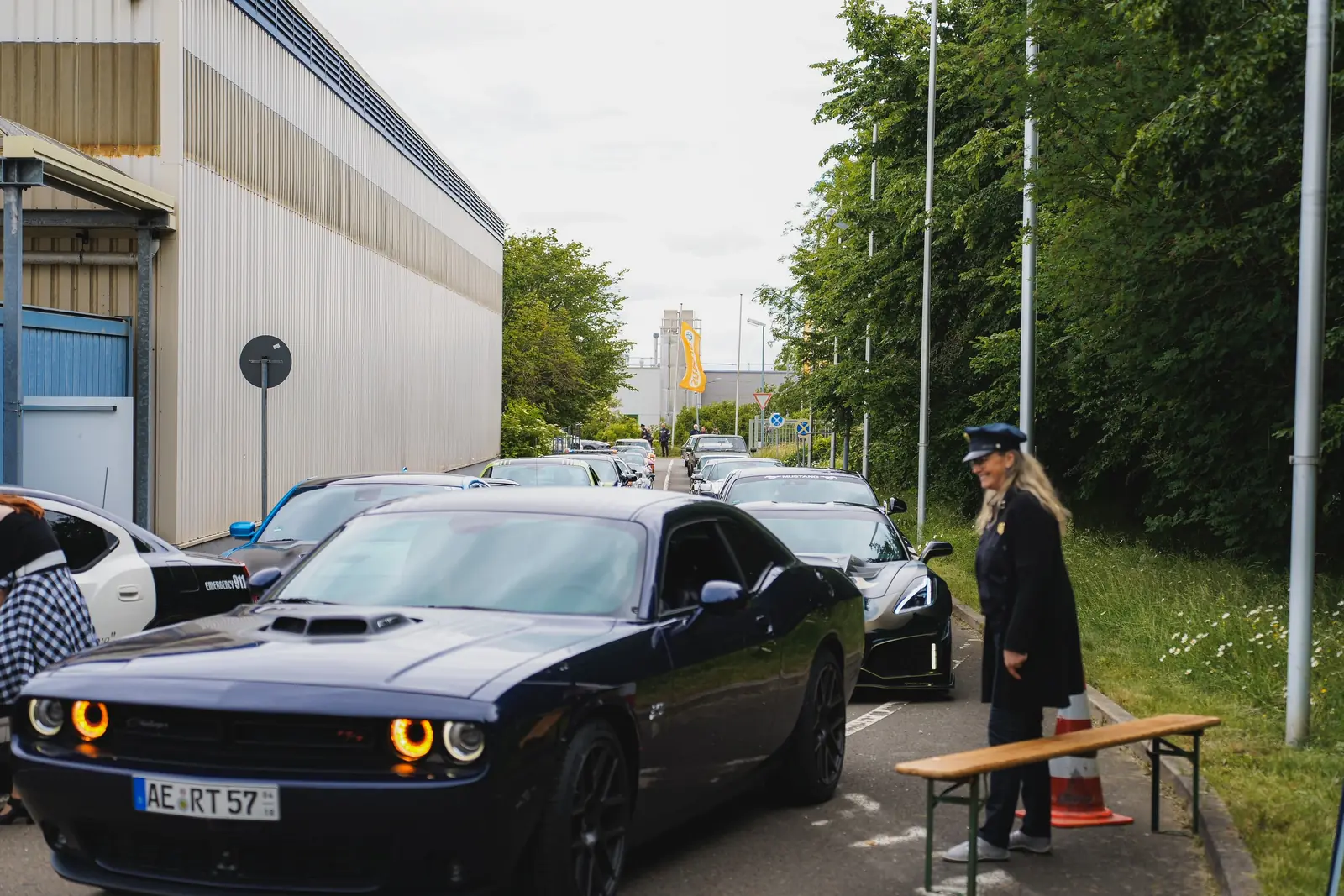 Dunkler Dodge Challenger an der Einfahrt, daneben eine Frau in Uniform