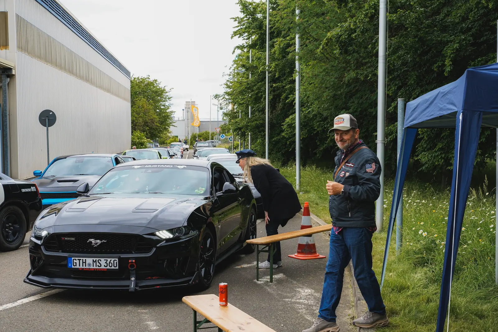 Schwarzer Mustang an der Einfahrt, ein Mann mit Basecap lacht in die Kamera