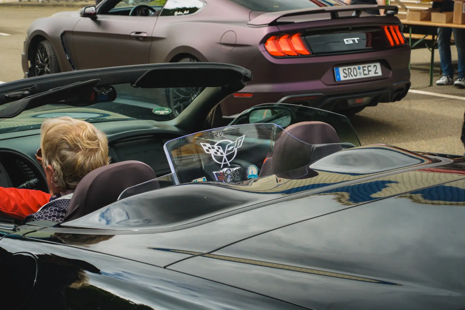 Besucherin in einem offenen Corvette-Cabrio, dahinter ein violetter Mustang