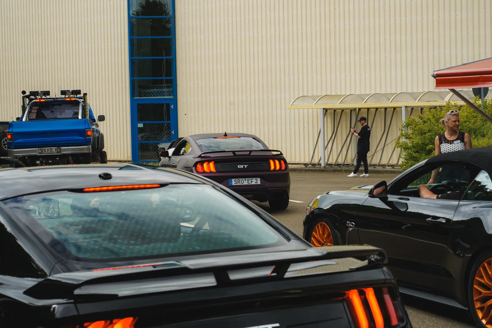 Schwarze Mustangs und ein blauer Pick-up vor der Halle