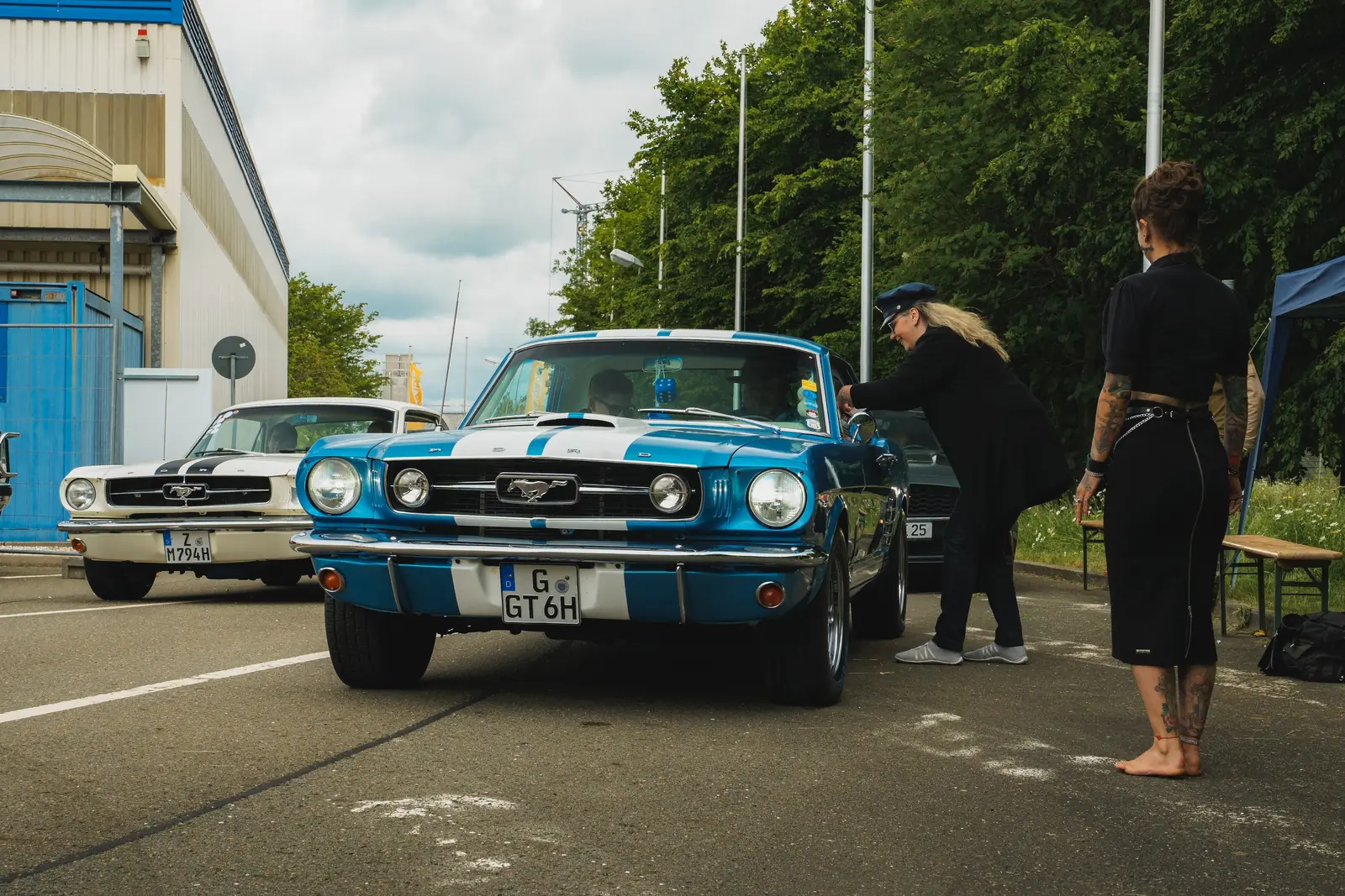 Blauer Mustang mit weißen Streifen an der Einfahrt, daneben zwei Frauen