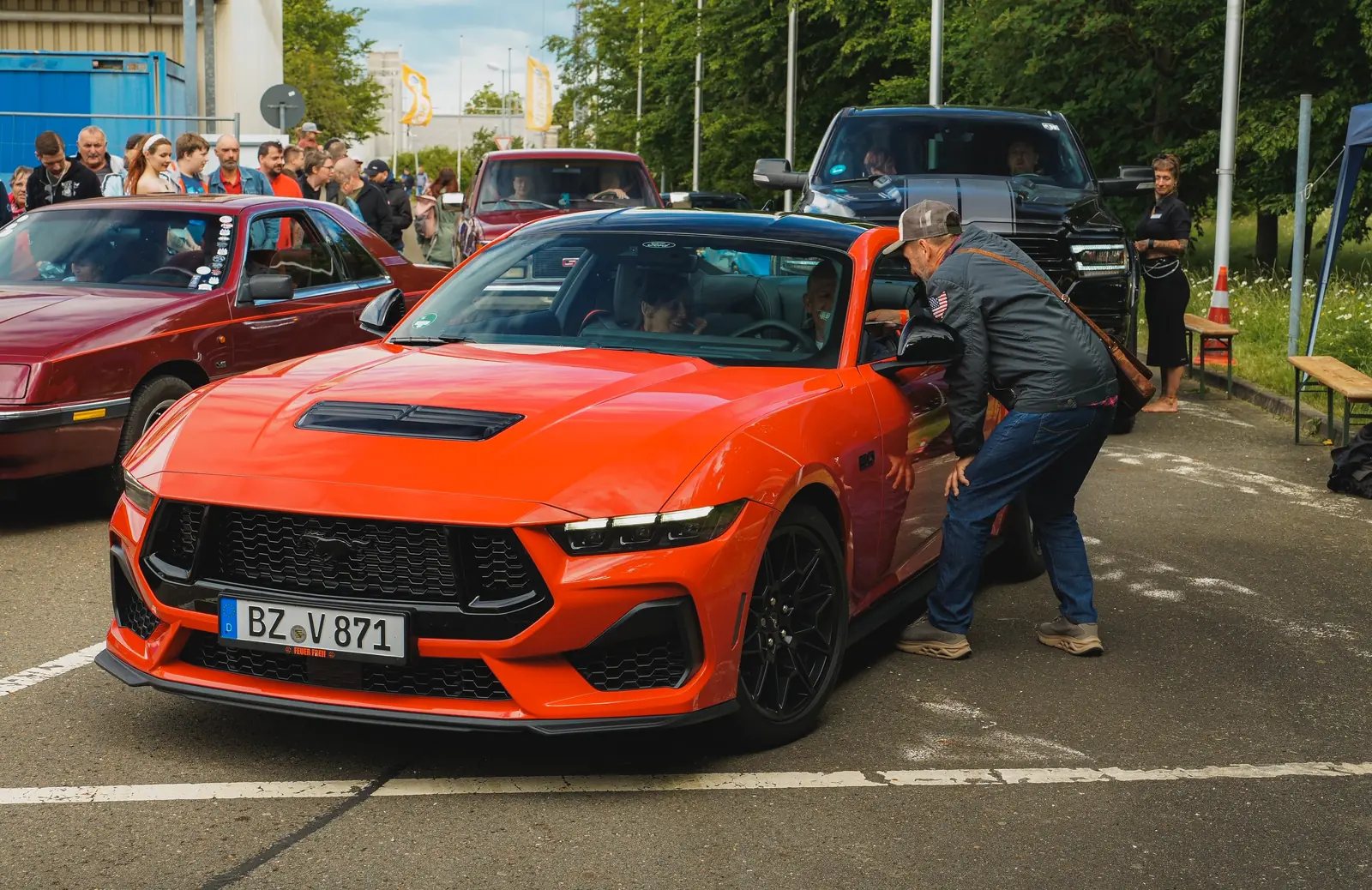 Oranger Mustang an der Einfahrt, ein Mann spricht mit dem Fahrer