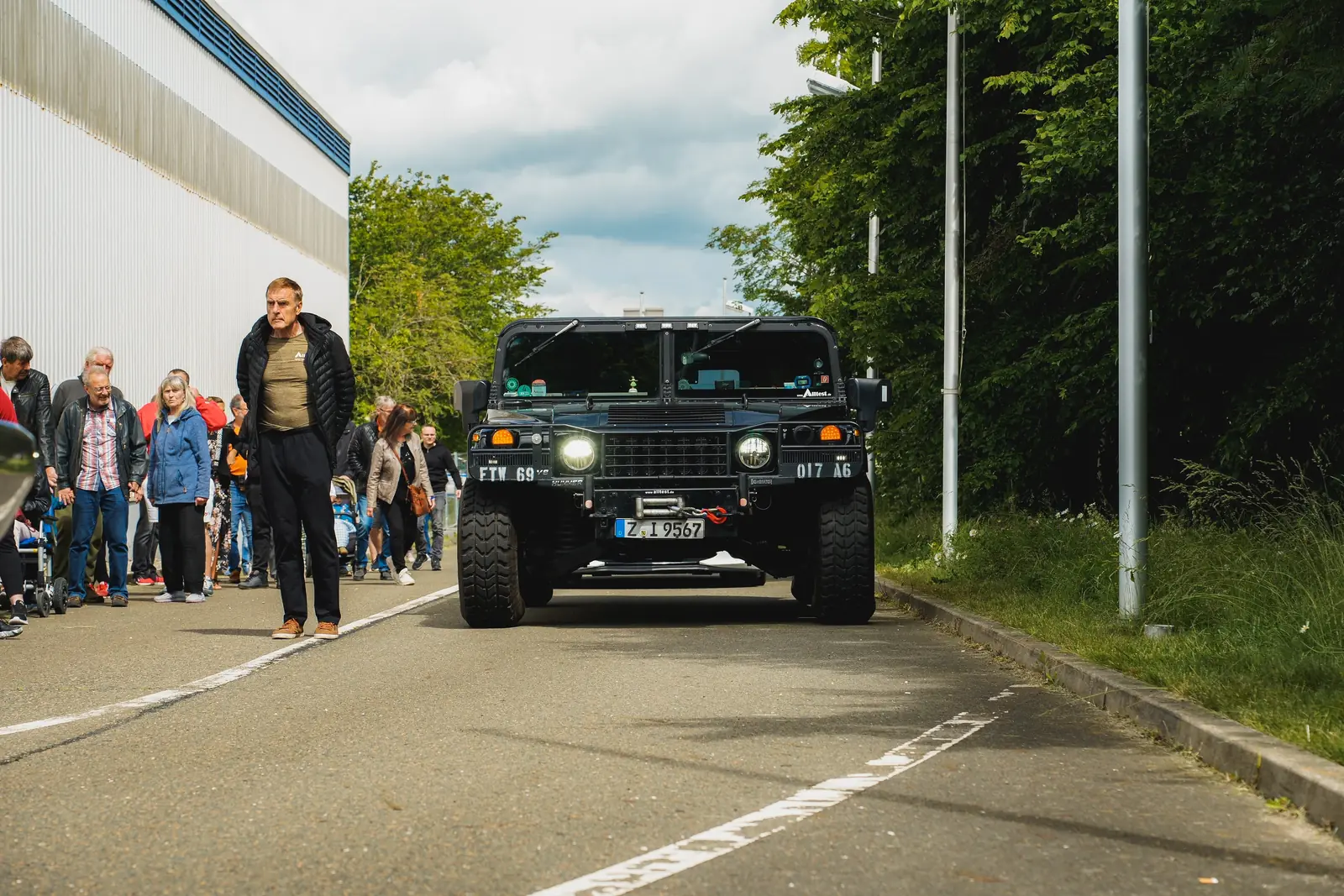 Schwarzer Hummer in der Zufahrt, am Rand wartende Besucher