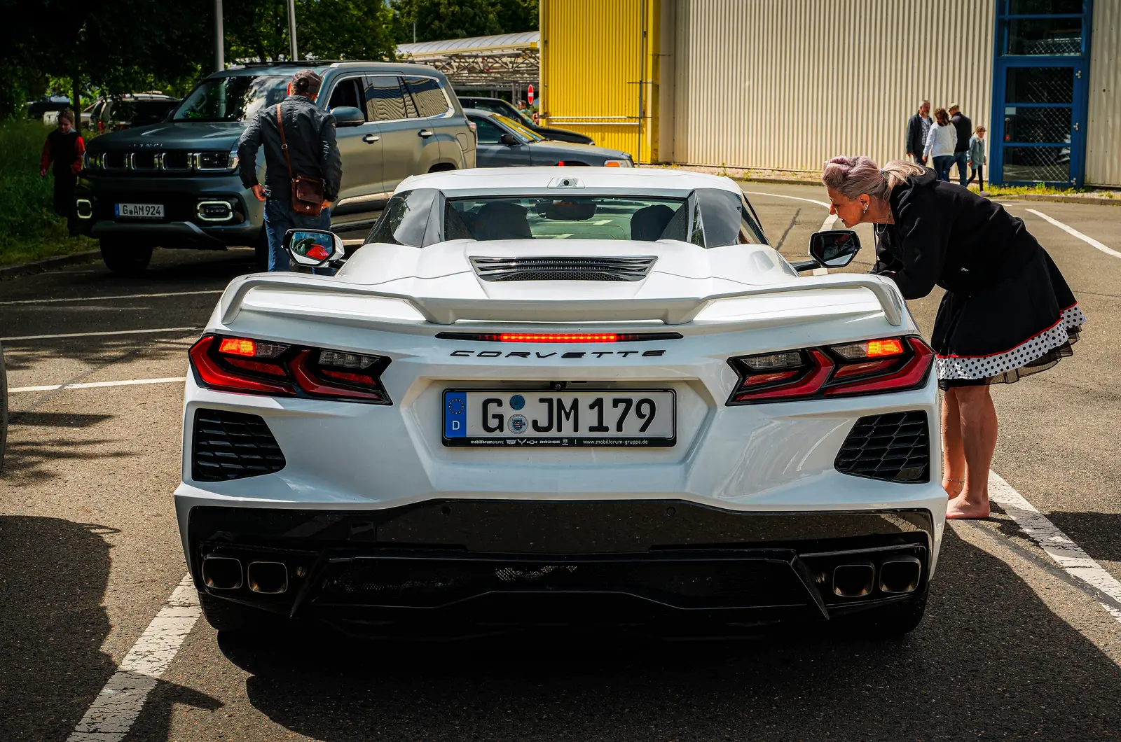 Weiße Corvette von hinten, eine Frau beugt sich zum Seitenfenster