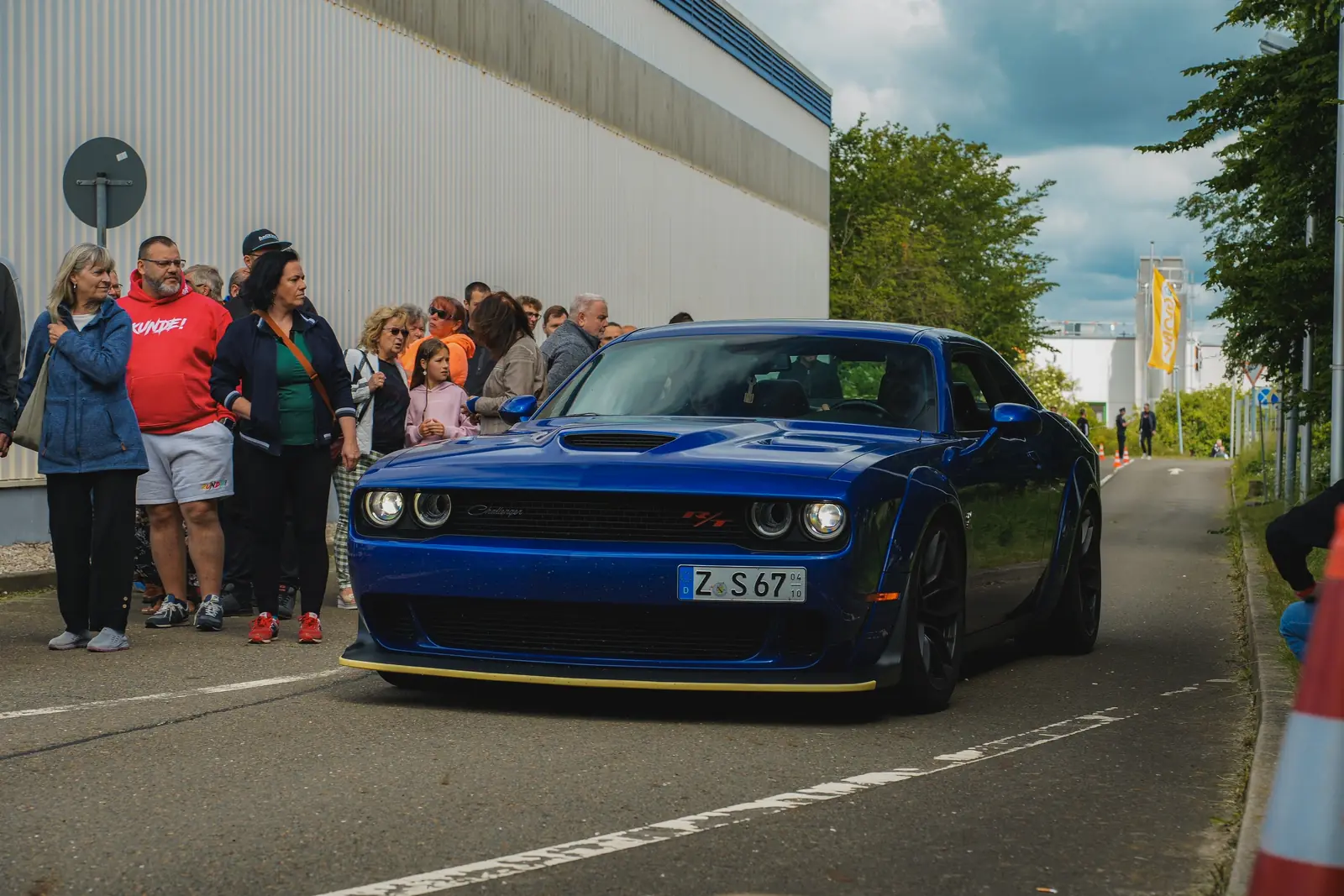 Blauer Dodge Challenger vor einer Reihe Besucher an der Hallenwand