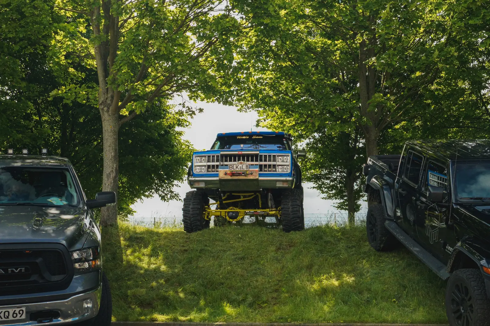 Blauer Pick-up mit Riesenrädern auf dem Grünstreifen zwischen Bäumen