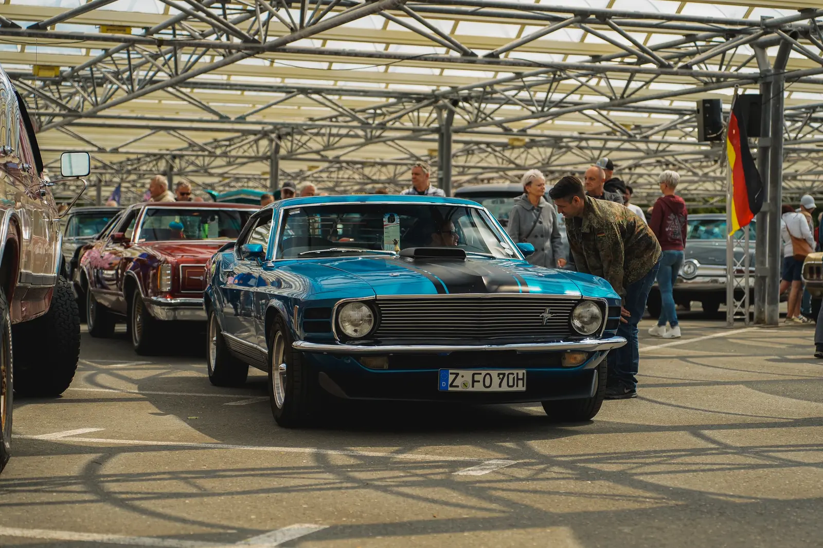 Blauer Mustang aus den Siebzigern unter dem Glasdach, Besucher schauen hinein