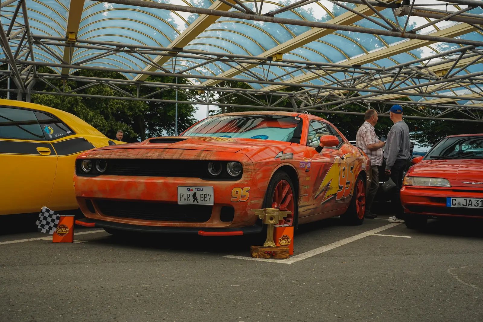 Dodge Challenger im Rostlook als Lightning McQueen, davor ein Pokal