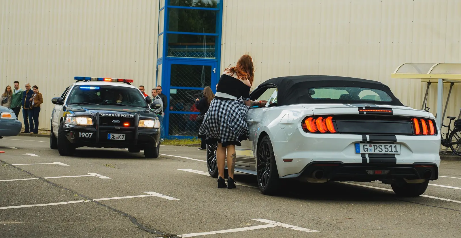 Polizeiwagen im Spokane-Look und weißer Mustang, eine Frau am Fenster