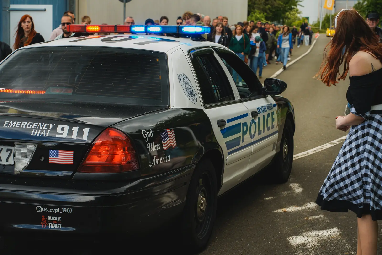 Heck des Polizeiwagens mit „Emergency Dial 911“, dahinter viele Besucher