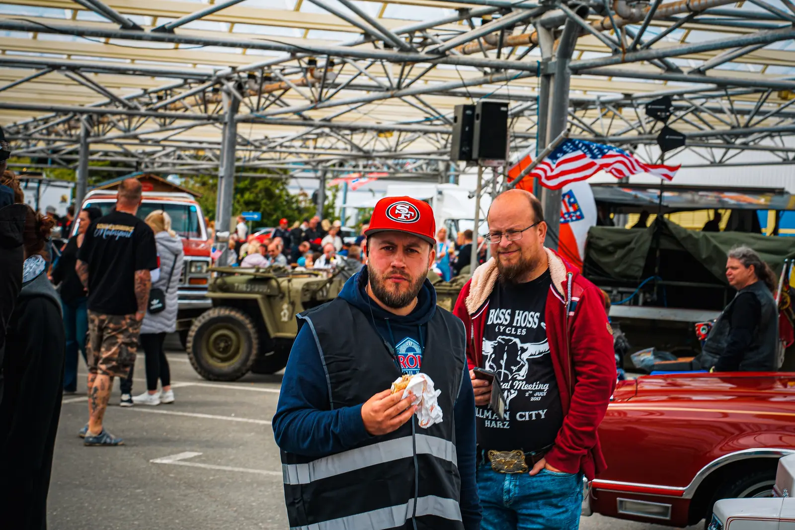 Zwei Besucher mit Imbiss unter dem Glasdach, hinten ein Willys-Jeep