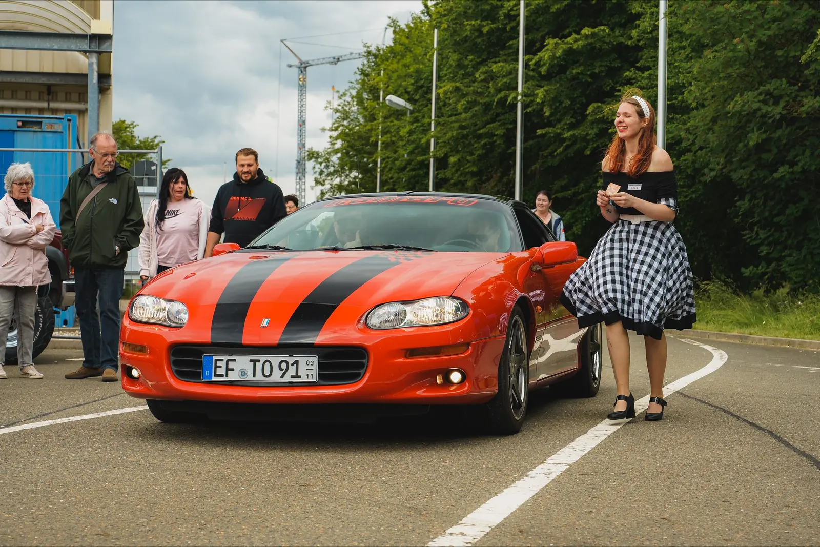 Oranger Camaro mit schwarzen Streifen, daneben eine Frau im Petticoat