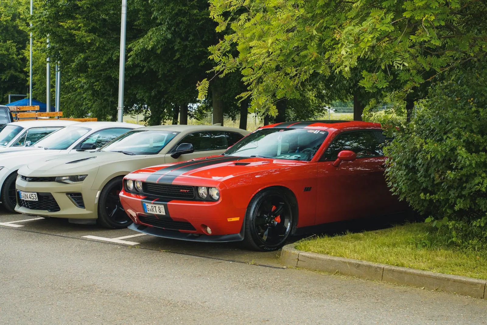 Roter Dodge Challenger und Camaro unter Bäumen geparkt