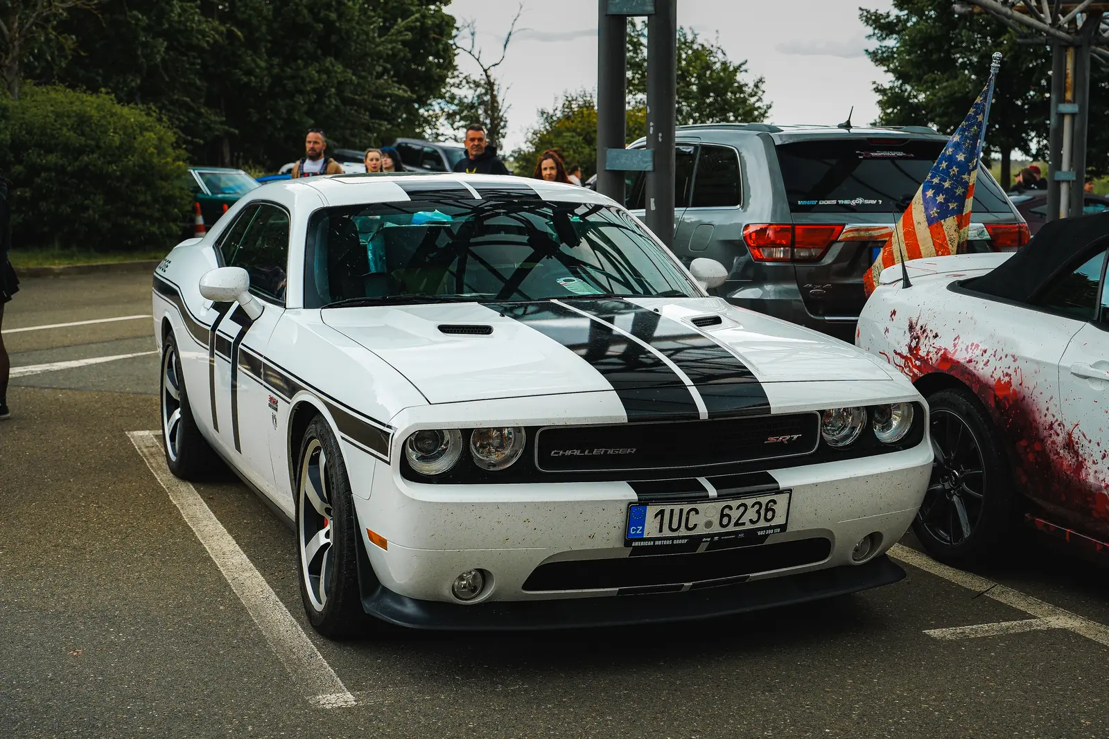 Weißer Dodge Challenger mit schwarzen Streifen, dahinter eine US-Flagge