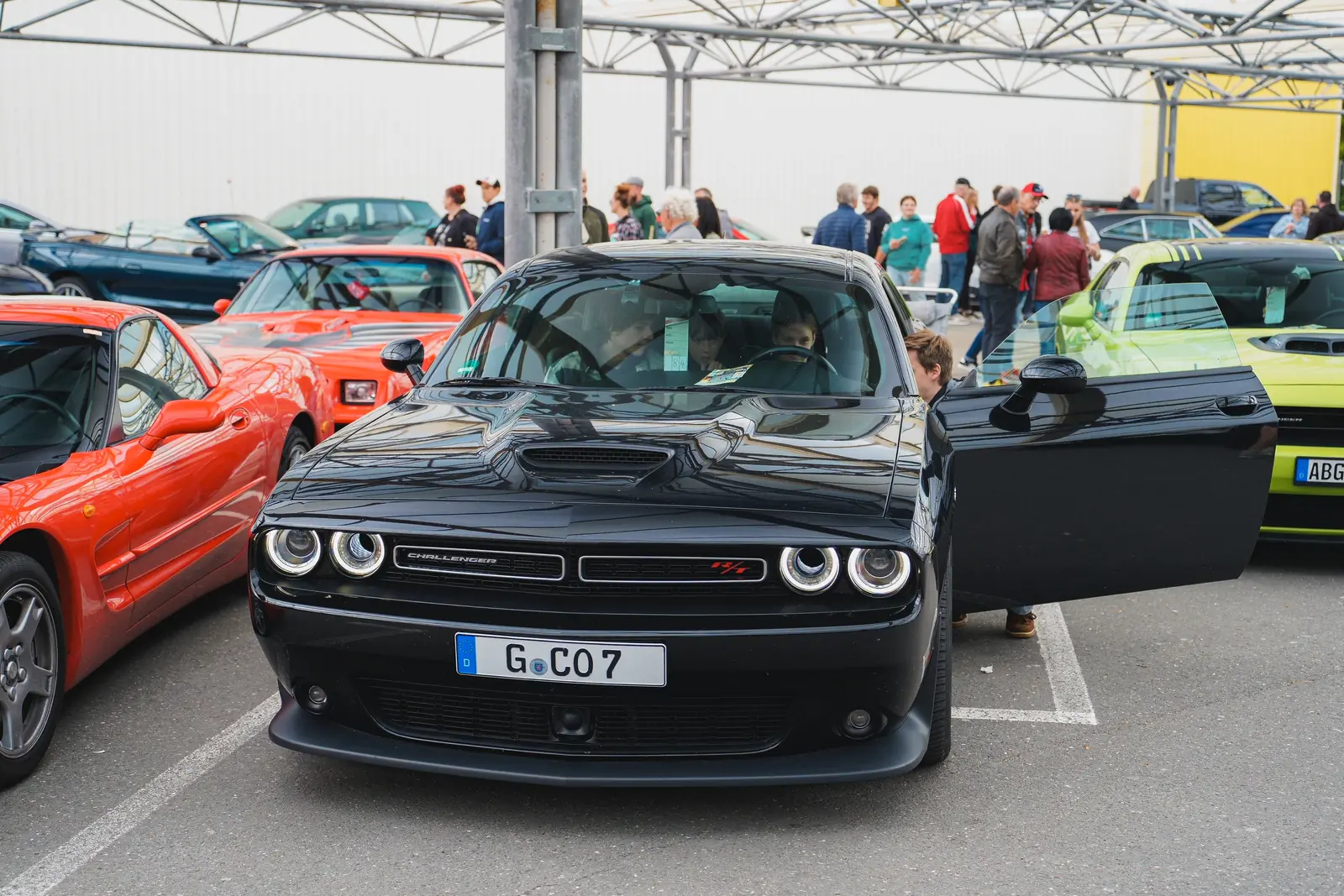 Schwarzer Dodge Challenger mit offener Tür neben einer roten Corvette