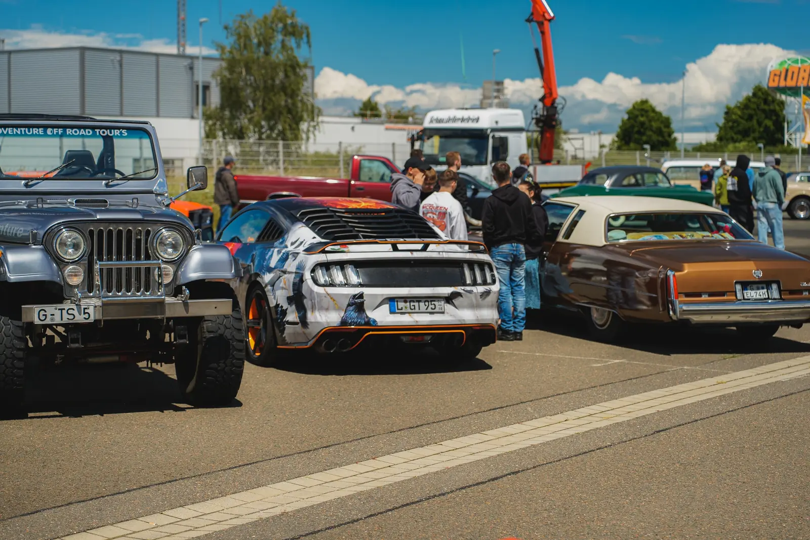 Jeep, Mustang mit Comic-Folierung und brauner Cadillac in der Sonne