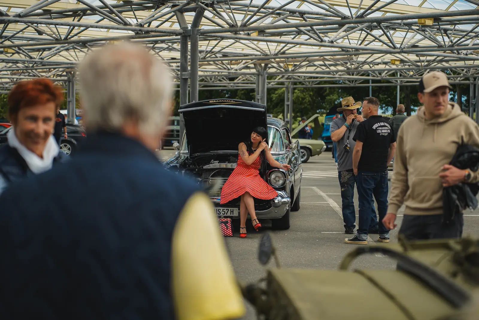 Frau im roten Kleid sitzt auf der Stoßstange eines Oldtimers