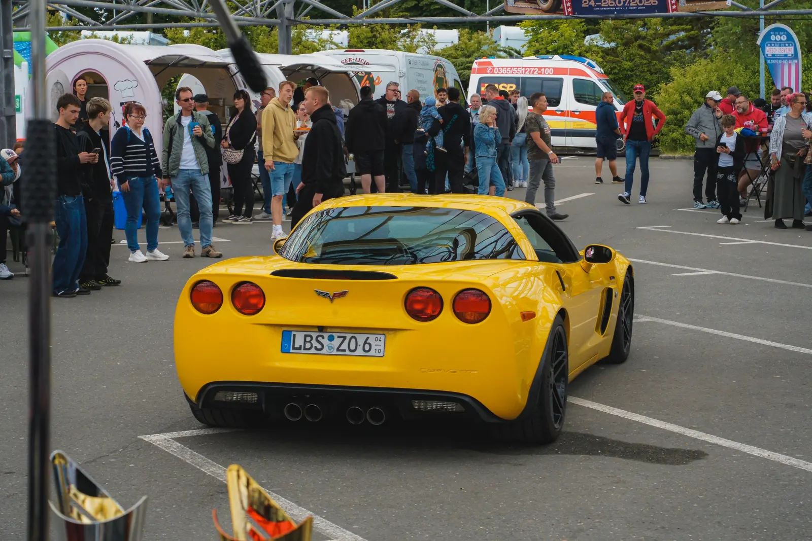 Gelbe Corvette rollt an vielen Besuchern vorbei, hinten Foodtrucks
