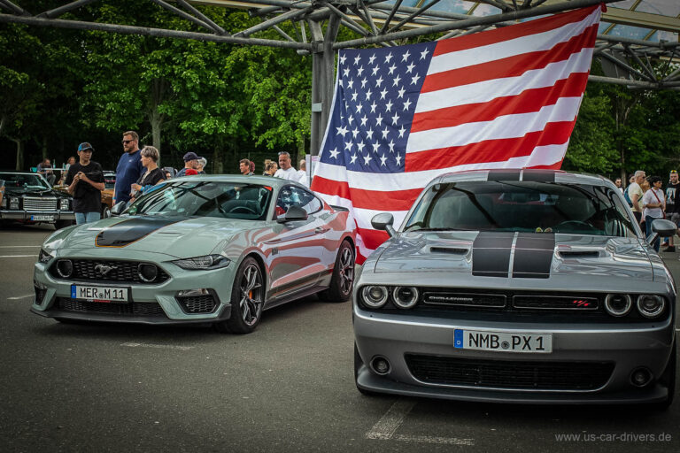 Grauer Mustang und Dodge Challenger vor einer großen US-Flagge