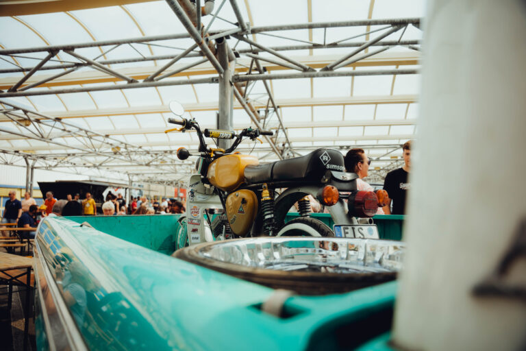 Türkiser Oldtimer im Vordergrund, dahinter Stände und ein Motorrad