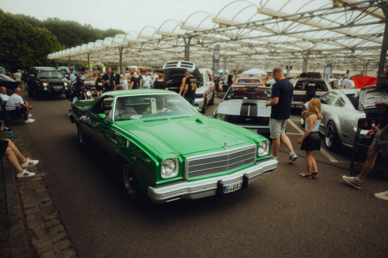 Grüner Chevrolet Monte Carlo rollt durch die Fahrzeugreihen