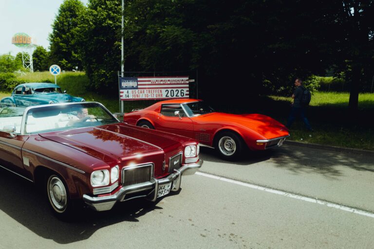 Weinroter Cadillac und rote Corvette am Platzrand